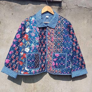 Può includere: Una giacca trapuntata blu con stampa floreale e bordatura a righe. La giacca ha due tasche a toppa e una chiusura con bottoni.
