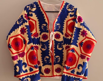 May include: A cream-colored jacket with a V-neck and long sleeves. The jacket is embroidered with a geometric pattern in shades of blue, red, and pink.