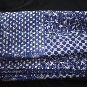 Puede incluir: Una colcha kantha azul y blanca con un dise&ntilde;o de patchwork. La colcha est&aacute; doblada y muestra diferentes patrones, incluyendo c&iacute;rculos, puntos y hojas.