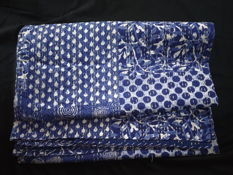 Puede incluir: Una colcha kantha azul y blanca con un dise&ntilde;o de patchwork. La colcha est&aacute; doblada y muestra diferentes patrones, incluyendo c&iacute;rculos, puntos y hojas.