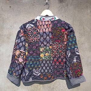 May include: A black quilted jacket with a patchwork design featuring various floral and geometric patterns in shades of pink, red, green, blue, and yellow. The jacket has a mandarin collar and long sleeves with a white and black striped trim.