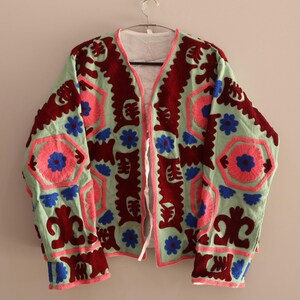 May include: A green jacket with intricate embroidery in shades of pink, blue, and maroon. The jacket has a V-neck and long sleeves.