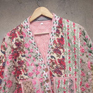 May include: A quilted jacket with a floral print in shades of pink, red, and white. The jacket has a V-neck and a button closure.