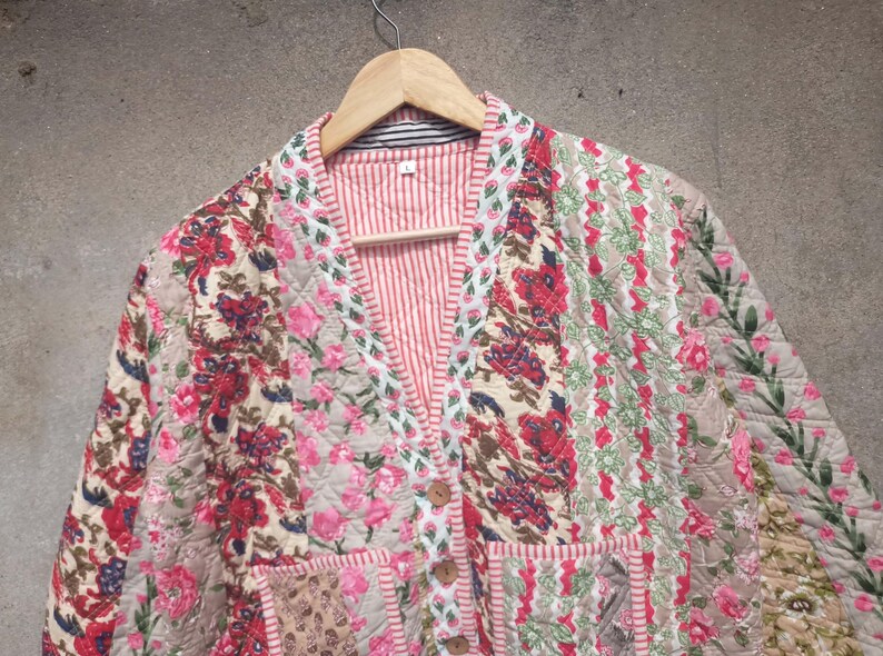 May include: A quilted jacket with a floral print in shades of pink, red, and white. The jacket has a V-neck and a button closure.