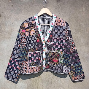 May include: A black quilted jacket with a floral patchwork design. The jacket has a button closure and two patch pockets. The fabric is a mix of black, white, pink, and green.