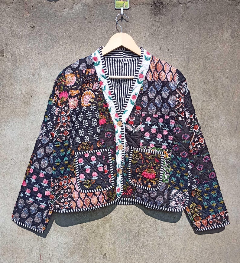 May include: A black quilted jacket with a floral patchwork design. The jacket has a button closure and two patch pockets. The fabric is a mix of black, white, pink, and green.