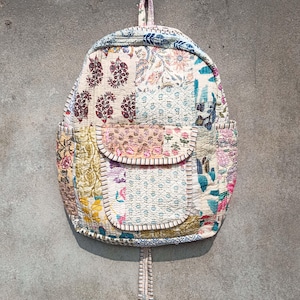 Peut inclure: Un sac à dos de style patchwork en tissu matelassé avec une variété de motifs floraux dans des tons de rose, bleu, vert et marron. Le sac à dos a une grande poche sur le devant et une fermeture à cordon.