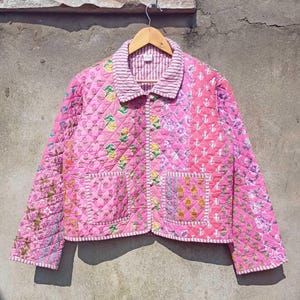 May include: A pink quilted jacket with a floral print and a button closure. The jacket has a collar and two pockets.
