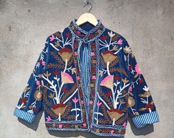 May include: A blue velvet jacket with embroidered floral designs in pink, white, and brown. The jacket has a mandarin collar and a button closure.