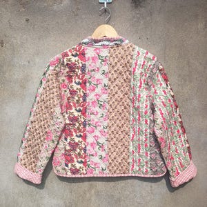 May include: A quilted jacket with a patchwork design featuring floral patterns in shades of pink, red, and brown. The jacket has a stand-up collar and a zipper closure.