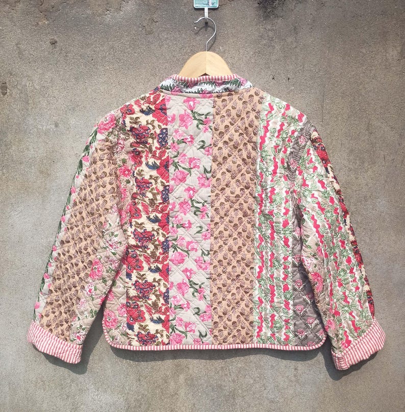 May include: A quilted jacket with a patchwork design featuring floral patterns in shades of pink, red, and brown. The jacket has a stand-up collar and a zipper closure.