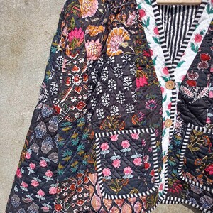 May include: A black quilted jacket with a floral print and a striped lining. The jacket has a button closure and a pocket on the left side.