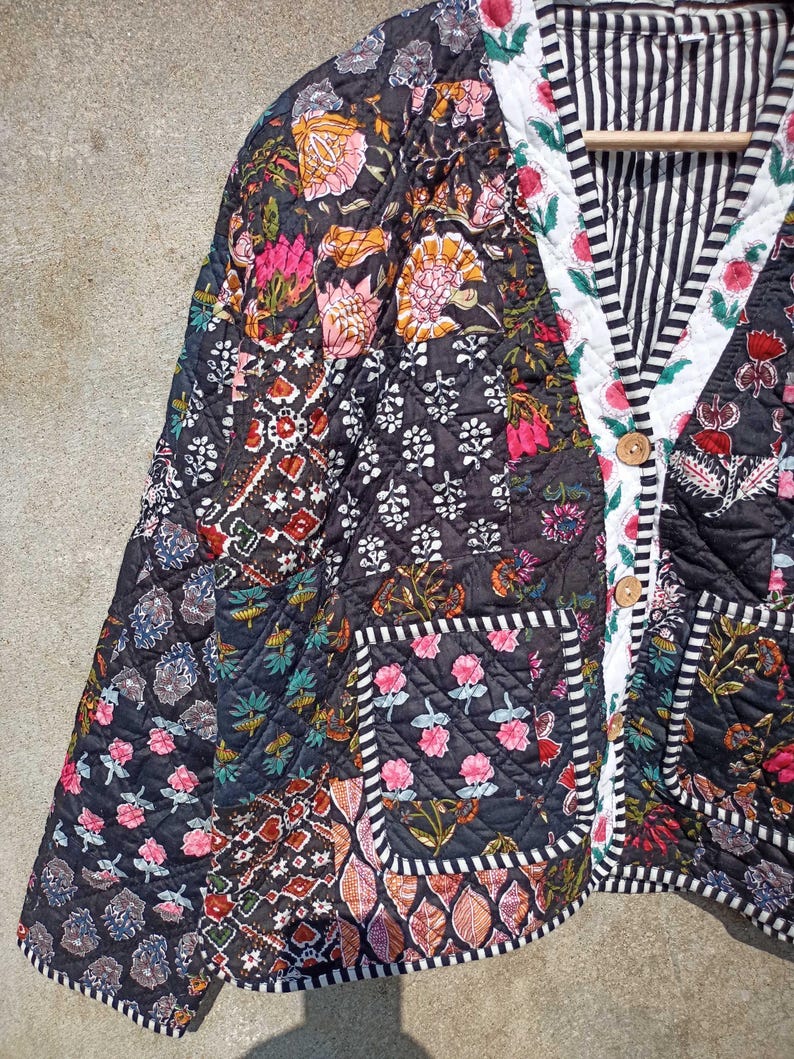 May include: A black quilted jacket with a floral print and a striped lining. The jacket has a button closure and a pocket on the left side.