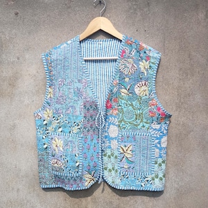 May include: A blue quilted vest with a floral print and a striped lining. The vest has a tie closure and a pocket on the front.