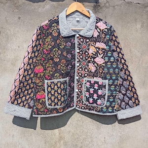 May include: A black quilted jacket with a floral print and a striped collar. The jacket has two patch pockets and a button closure.