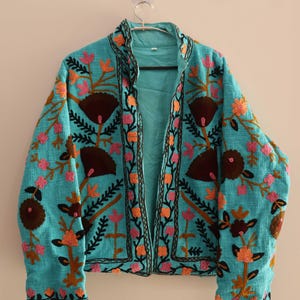 May include: A turquoise blue jacket with intricate floral embroidery in shades of pink, orange, brown, and black. The jacket has a mandarin collar and a front closure.