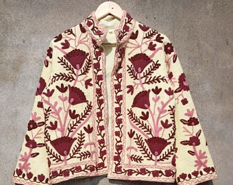 May include: A cream-colored jacket with a mandarin collar and long sleeves. The jacket is embroidered with a floral pattern in shades of burgundy and pink.