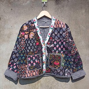 May include: A black quilted jacket with a floral patchwork design. The jacket has a button closure, two pockets, and a striped lining.