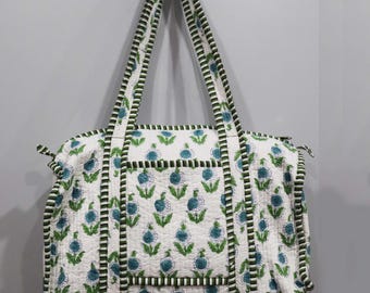 Könnte beinhalten: Eine weiße Baumwoll-Tragetasche mit einem grünen und blauen Blumendruck. Die Tasche hat zwei lange Henkel und einen Reißverschluss.