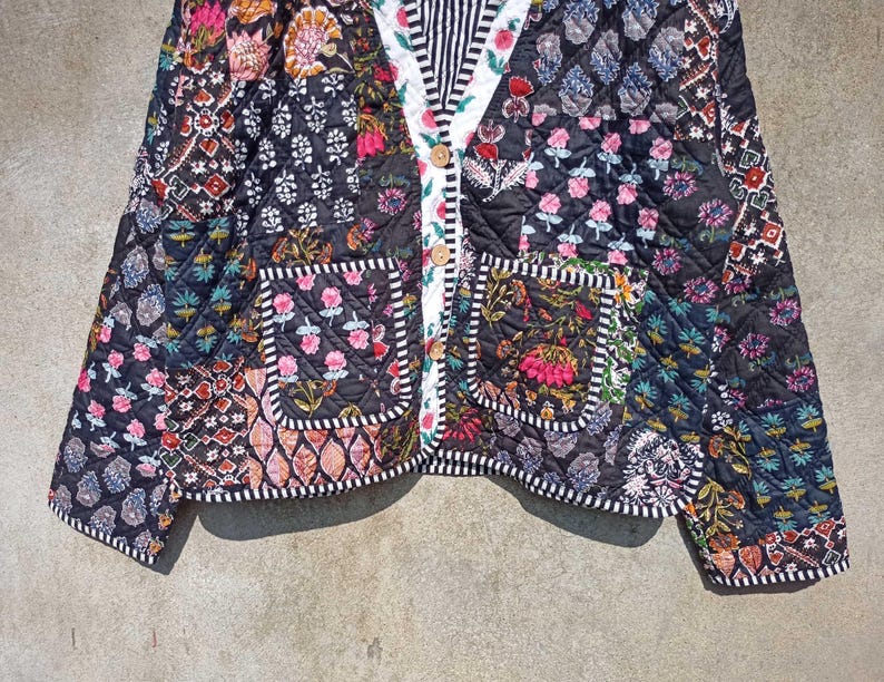 May include: A black quilted jacket with a patchwork design featuring floral and geometric patterns. The jacket has a button closure, two pockets, and a white and black striped trim.