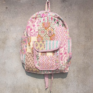 Può includere: Uno zaino in stile patchwork realizzato in tessuto trapuntato in tonalità rosa, bianco e marrone. Lo zaino ha un ampio scomparto principale e una tasca anteriore più piccola. Gli spallacci sono regolabili e si legano in cima.