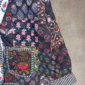 May include: A black quilted jacket with a patchwork design featuring various floral patterns. The jacket has a striped trim and a pocket on the left side.