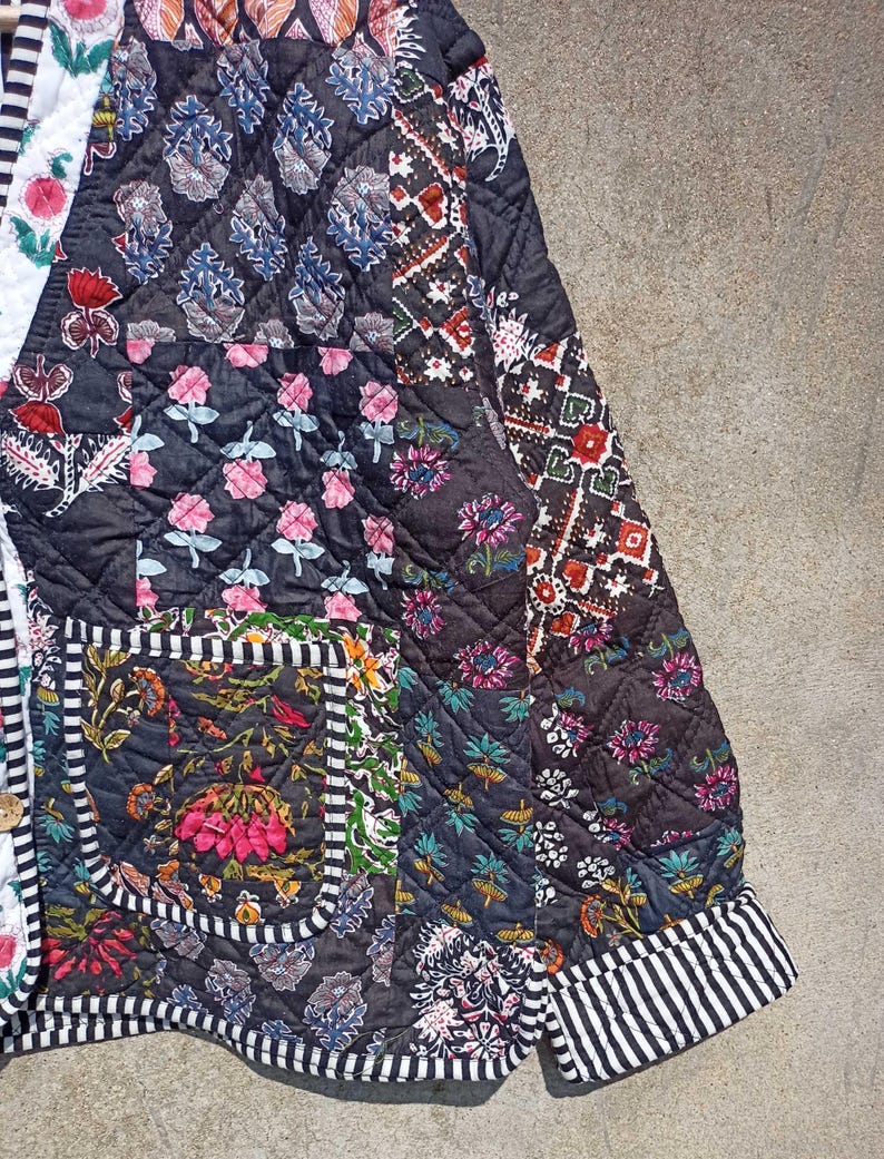 May include: A black quilted jacket with a patchwork design featuring various floral patterns. The jacket has a striped trim and a pocket on the left side.