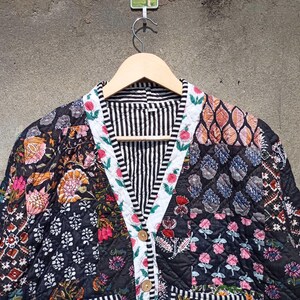 May include: A black and white quilted jacket with a floral print. The jacket has a V-neck and a button closure. The fabric is patchwork and features a variety of floral patterns.