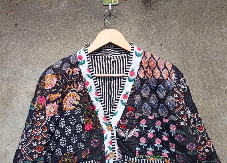 May include: A black and white quilted jacket with a floral print. The jacket has a V-neck and a button closure. The fabric is patchwork and features a variety of floral patterns.