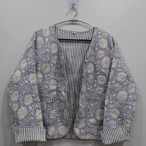 May include: A blue quilted jacket with a white floral print. The jacket has a striped lining and two pockets.