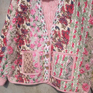 May include: A quilted jacket with a floral print in shades of pink, red, and green. The jacket has a V-neck, two pockets, and a button closure.