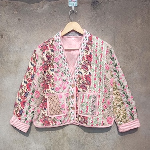 May include: A quilted jacket with a floral print in shades of pink, white, and green. The jacket has a button closure and two pockets.