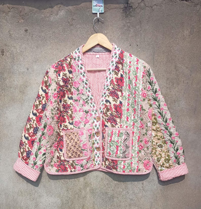 May include: A quilted jacket with a floral print in shades of pink, white, and green. The jacket has a button closure and two pockets.
