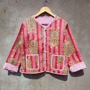 May include: A pink and white striped quilted jacket with a tiger print. The jacket has a button closure and two pockets.