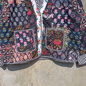 May include: A black quilted jacket with a patchwork design featuring floral and geometric patterns. The jacket has a button closure and two patch pockets.