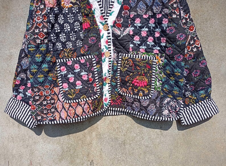 May include: A black quilted jacket with a patchwork design featuring floral and geometric patterns. The jacket has a button closure and two patch pockets.