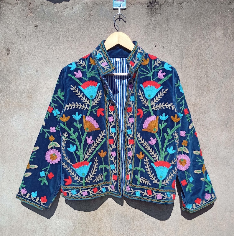 Op de afbeelding: Een donkerblauw fluwelen jasje met kleurrijke bloemenborduursel. Het jasje heeft een knoopsluiting aan de voorkant en lange mouwen.