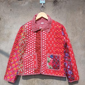 May include: A red quilted jacket with a patchwork design. The jacket has a button closure and a collar. The fabric is a mix of floral and geometric patterns.