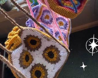 May include: Three crocheted bags hanging from a window. The top bag is red, blue, and yellow. The middle bag is pink and purple. The bottom bag is white, brown, and yellow with a sunflower pattern.
