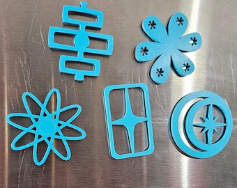 May include: Five blue metal refrigerator magnets with geometric designs. The magnets are in the shape of a star, a circle, a rectangle, a flower, and a geometric design. The magnets are on a stainless steel refrigerator with a "Smile More" sticker.