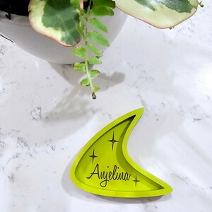 Op de afbeelding: Een felgroene, halvemaanvormige dienblad met de naam "Angelina" gegraveerd in zwarte letters. Het dienblad heeft een retro, mid-century modern design en twee kleine sterren aan weerszijden van de naam.