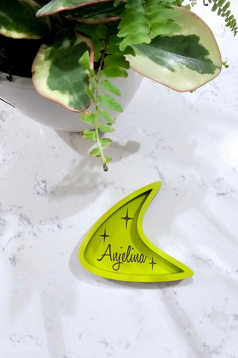Op de afbeelding: Een felgroene, halvemaanvormige dienblad met de naam "Angelina" gegraveerd in zwarte letters. Het dienblad heeft een retro, mid-century modern design en twee kleine sterren aan weerszijden van de naam.