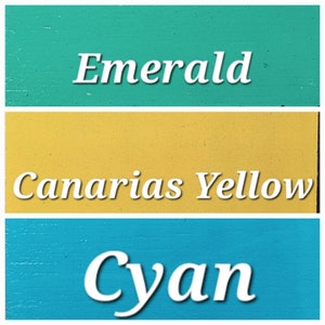 Op de afbeelding: Drie verfkleuren met de namen "Emerald", "Canarias Yellow" en "Cyan" in wit.
