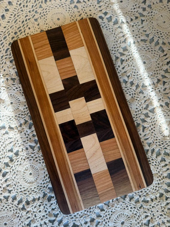 Cutting board built from a mosaic of inlaid wood pieces — it's functional kitchen art that looks like a parquet floor, not a kitchen tool.