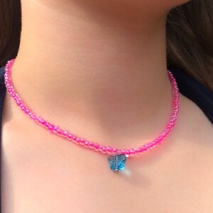 May include: A pink beaded choker necklace with a blue butterfly charm.