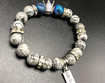 May include: Grey stone beaded bracelet with a silver crown charm and a silver tag that says "Otelo".