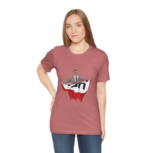 May include: A woman wearing a mauve t-shirt with a graphic of a man holding a red and white flag with a black swastika.