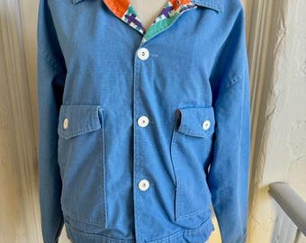 May include: A blue denim jacket with a colorful patterned lining. The jacket has a button closure and two large pockets on the front.