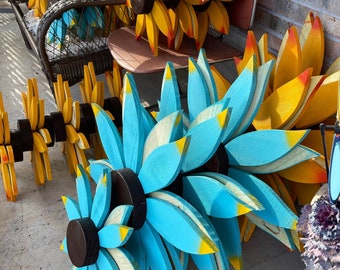 May include: A collection of wooden flower wall decor in blue and yellow. The flowers are made of individual wooden pieces that are painted and assembled to create a 3D effect.