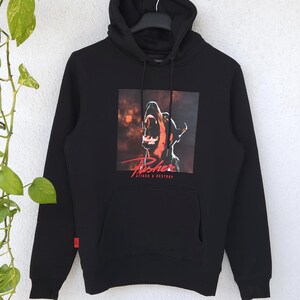 Könnte beinhalten: Ein schwarzer Kapuzenpullover mit einem Grafikdruck eines knurrenden Dobermanns und dem roten Schriftzug "Pusher" sowie "ATTACK & DESTROY" darunter. Der Hoodie verfügt über eine Kängurutasche, lange Ärmel und ein kleines rotes Etikett.